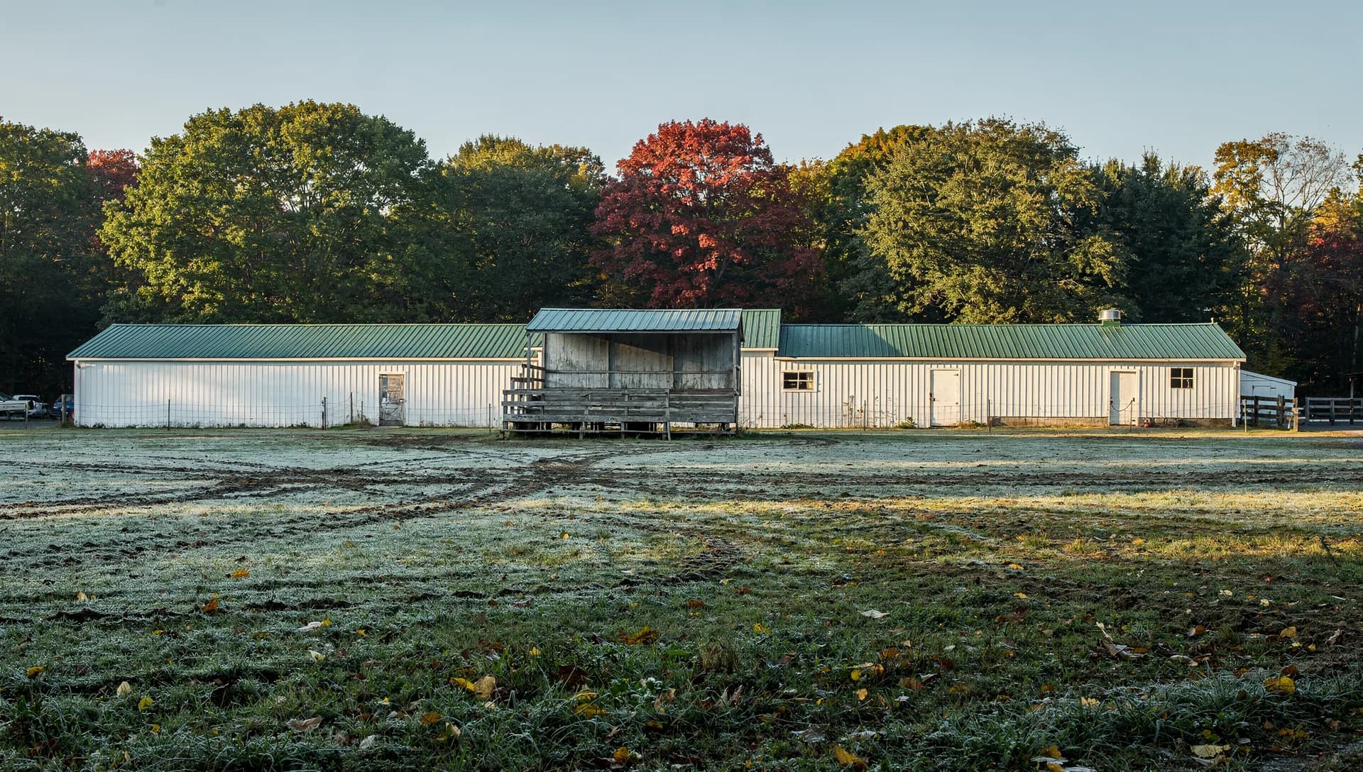 Long white livestock barns with green roofs and a small wooden grandstand stand over frosted grass.