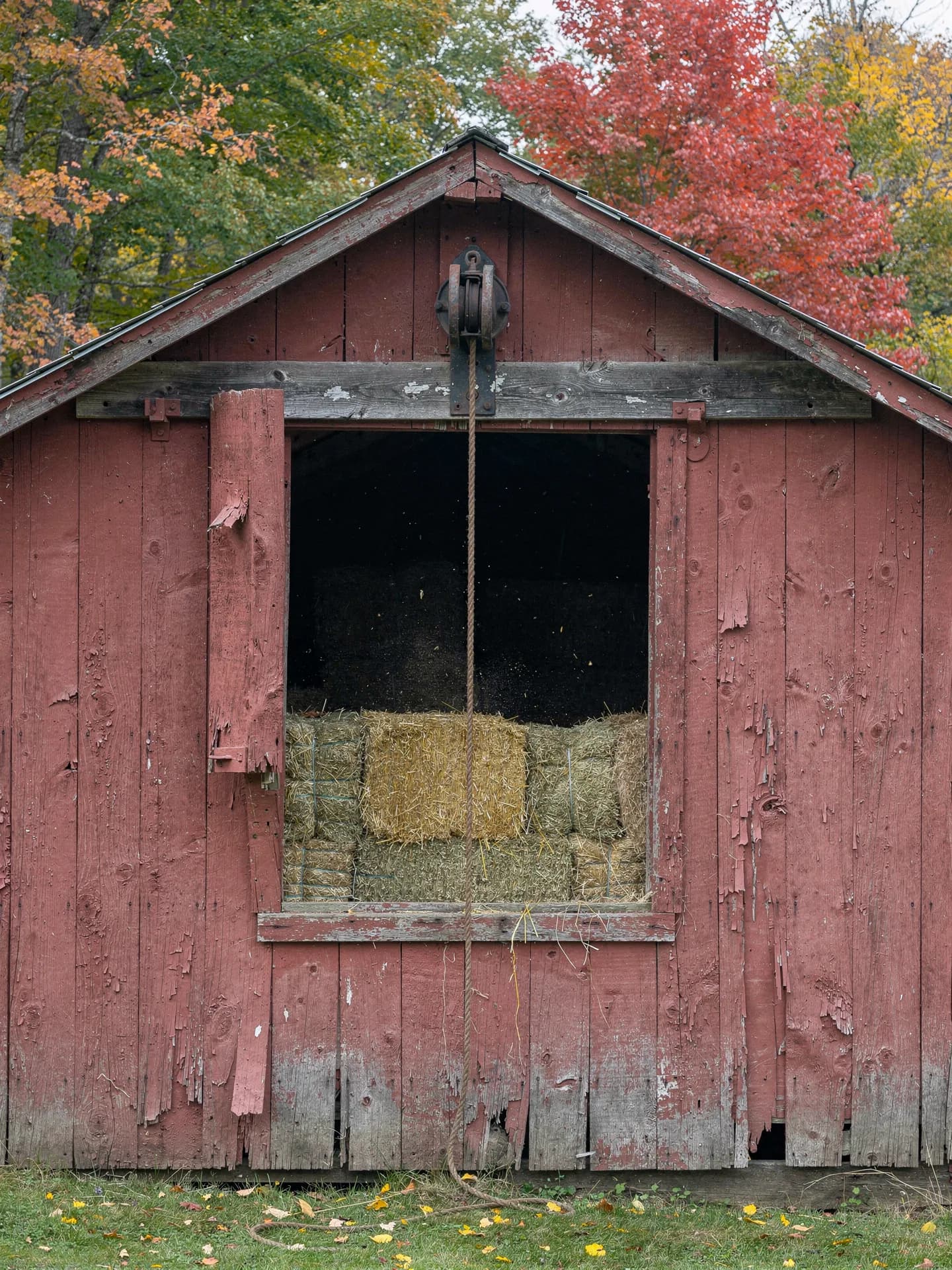 Hay bales fill the open loft door in the gable of an old red barn, an iron pulley and rope hanging from the beam above.